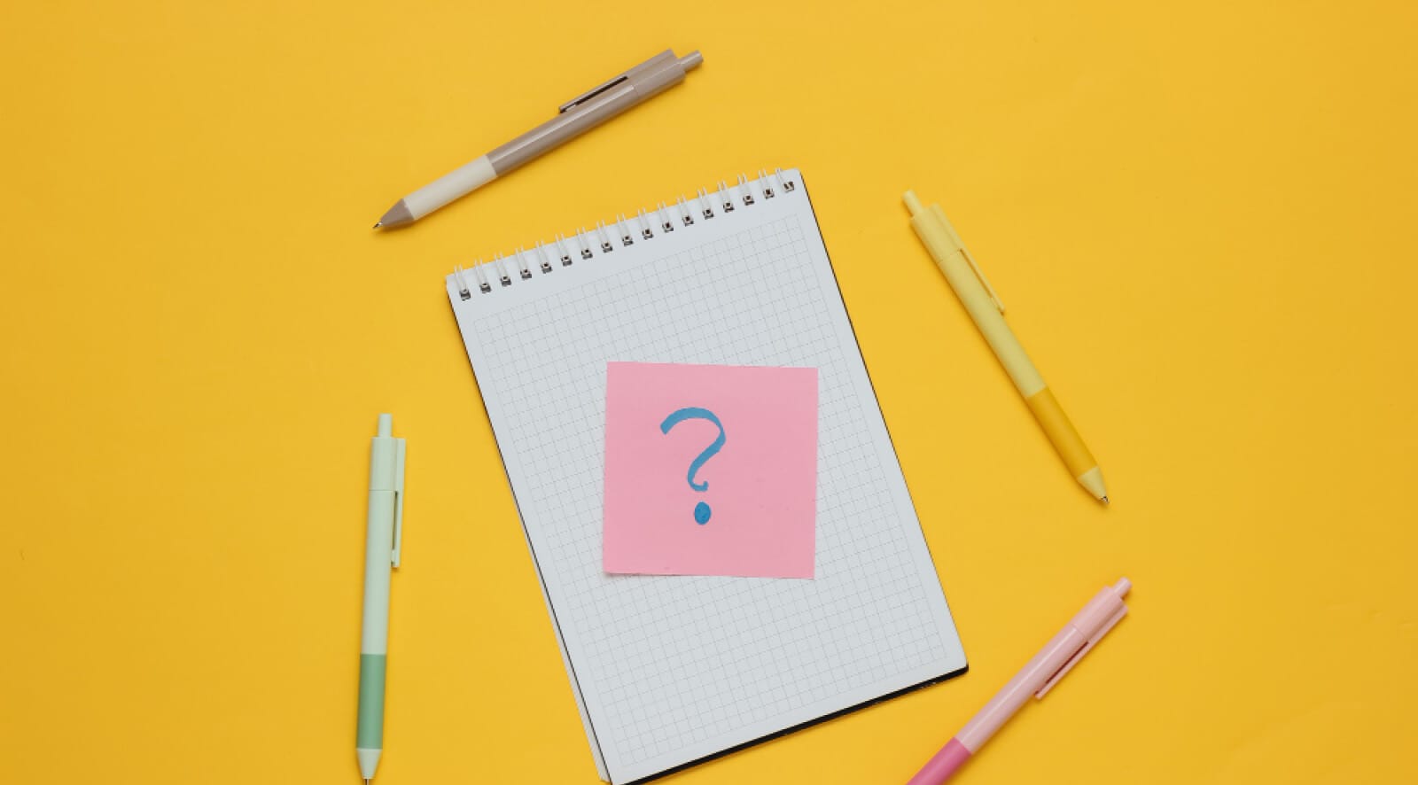 Notebook with a question mark on it, surrounded with pens